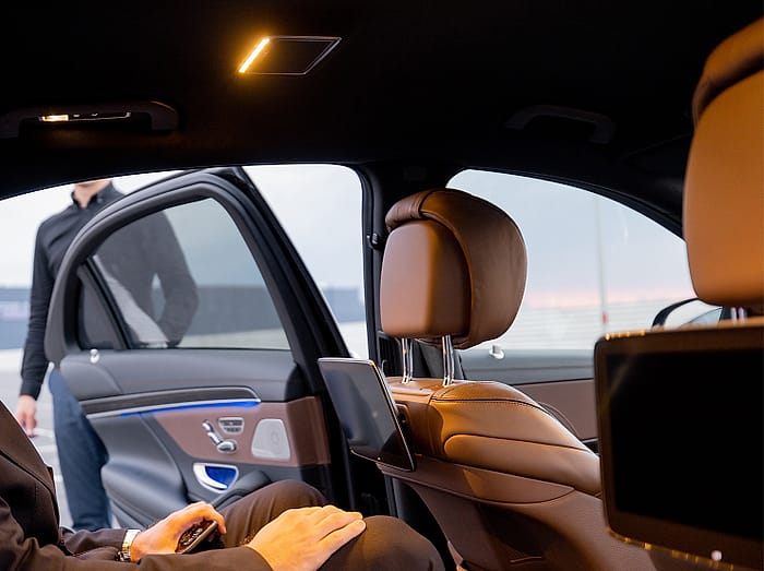 Rear seat of a luxury vehicle with leather headrests and seat-back screens, door open