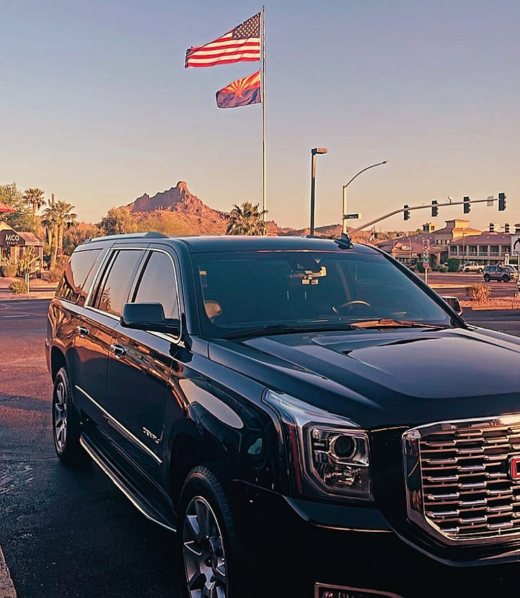 Black GMC Yukon XL Denali parked under the US and Arizona flags with a desert peak behind, Scottsdale