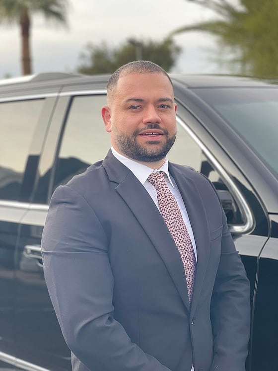 Ergi Janku, CEO and Managing Director of Comfort Luxury Rides, in a suit beside a black SUV